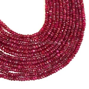May include: Close-up of multiple strands of ruby gemstone beads. The beads are a deep red color and have a faceted cut, creating a sparkling effect. The strands are arranged in a cascading pattern against a white background.