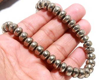 May include: A beaded bracelet made of metallic, silver-colored beads. The beads are cylindrical and strung together to form a flexible bracelet. The bracelet is held in a hand against a white background.