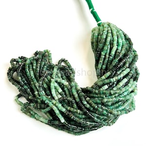 May include: A collection of emerald green gemstone beads. The beads are small, cylindrical, and strung on a green cord. The beads vary in shade, with some appearing darker. The background is white, highlighting the beads' colour and texture.