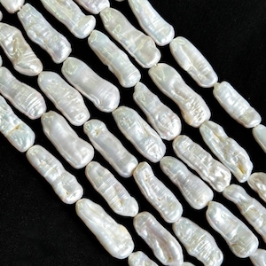 May include: Close-up of multiple strands of white, oblong, baroque pearls. The pearls have a lustrous, iridescent sheen and are strung together, creating a textured surface against a black background. These pearls are ideal for jewelry making.