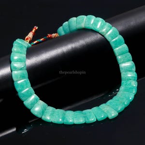 May include: A turquoise Amazonite bracelet. The bracelet is made of rectangular, polished stones strung together. The ends are tied with a colorful cord. The background is black. The text "thepearlshopin" is visible on the right side.