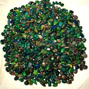 May include: A pile of black opal gemstones in diverse shapes. The opals exhibit a vibrant play-of-colour, with flashes of green, blue, red, and gold. The gemstones are scattered, creating a rich and textured appearance.