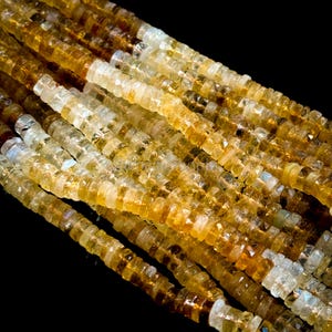 May include: Close-up of strands of citrine gemstone beads. The beads are a mix of golden yellow and clear, with a faceted, disc-like shape. The beads are strung together, creating a textured and shimmering effect against a black background.