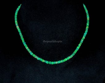 May include: A necklace composed of small, circular, vibrant green opal beads that display iridescent flashes of color. The text thepearlshopin is visible in the center of the necklace. The beads are strung together in a single strand.