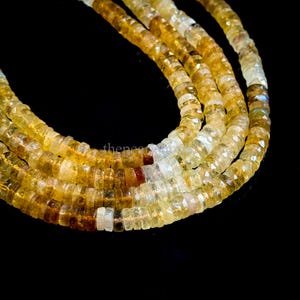 May include: Close-up of strands of faceted gemstone beads in shades of yellow, amber, and clear. The beads are small and uniform in size, strung together to form a necklace or bracelet. The background is black, highlighting the colors of the gemstones.
