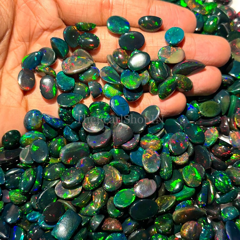 May include: A selection of polished black opal gemstones, displaying flashes of green, blue, and red. The opals are in various shapes and sizes, highlighting their unique colour play. These gemstones are suitable for jewellery making.