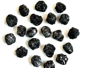 May include: A collection of rough, black gemstones with a textured surface, scattered on a white background. The stones vary in size and shape, with a slightly reflective quality. The overall arrangement is visually appealing.