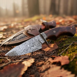 May include: A Damascus steel hunting knife with a dark wooden handle and a leather sheath. The blade has a unique swirling pattern. The sheath is brown with decorative stitching and a strap. The knife is resting on a bed of leaves.