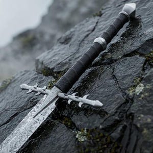 May include: A metal sword featuring a long, textured blade and a crossguard with decorative, thorn-like protrusions. The handle is wrapped in black material, accented by silver-colored metal rings and a pointed, faceted pommel at the end.