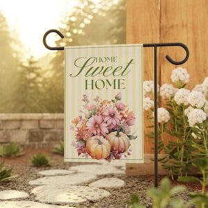 Könnte beinhalten: Eine rechteckige Gartenflagge mit einem Hintergrund aus vertikalen gelben und weißen Streifen. Der Text HOME Sweet HOME ist in Dunkelgrün gedruckt. Unter dem Text befindet sich ein Blumenarrangement aus rosa und orangefarbenen Blüten.