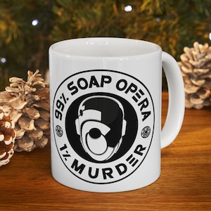 May include: White ceramic mug with a black and white graphic. The graphic features a stylized face within a circle, surrounded by the words "99% Soap Opera 1% Murder."