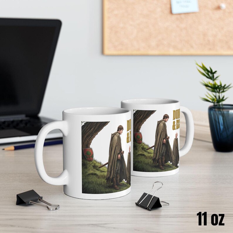 Może przedstawiać: Biały ceramiczny kubek z czarnym uchwytem i napisem "But First, Coffee" pogrubioną, czarną czcionką. Kubek jest umieszczony na rozmytym tle, sugerującym przytulne otoczenie. Kubek ma około 10 cm wysokości.