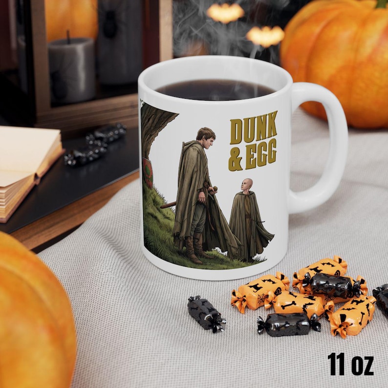 Może przedstawiać: Biały ceramiczny kubek z czarnym uchwytem i napisem "But First, Coffee" czarną, odręczną czcionką. Kubek stoi na białej powierzchni.