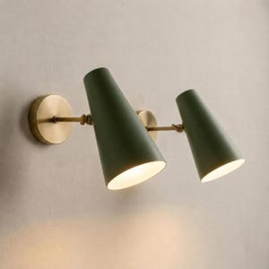 Könnte beinhalten: Zwei Wandleuchten mit olivgrünen, konischen Schirmen und Messingbeschlägen. Das Design ist minimalistisch, mit kreisförmigen Wandplatten, schlanken Armen und abgewinkelten Schirmen. Die Schirme haben einen Durchmesser von ca. 15 cm.