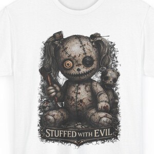 May include: White t-shirt featuring a distressed graphic of a stitched doll with one button eye and a wrench. The doll is holding a wrench and has a smaller doll behind it. The text "STUFFED WITH EVIL" is below the graphic.