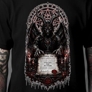 May include: A black t-shirt featuring a graphic print of a horned, winged figure holding a scroll labeled INFERNAL PACT, YOUR SOUL FOR MY FAVORS. The design includes red candles, a circular occult symbol, and dripping details in red and white ink.