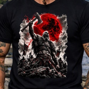 Może przedstawiać: Czarny t-shirt z nadrukiem graficznym przedstawiającym wojownika unoszącego topór na tle wielkiego czerwonego księżyca i ciemnych chmur. Wzór zawiera sylwetki innych postaci w oddali, utrzymane w odcieniach czerwieni, czerni i bieli.