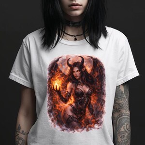 Può includere: T-shirt bianca con un'illustrazione fantasy di un demone femminile con corna, ali e un'aura di fuoco. L'opera d'arte è centrata sulla maglietta. La persona indossa un choker nero e ha tatuaggi sulle braccia.