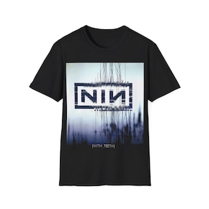 May include: Black t-shirt featuring the band name "NIN" in a rectangular frame, with a blurred blue and white background. The text "[WITH TEETH]" is below the image. The shirt is a short-sleeved crew neck.