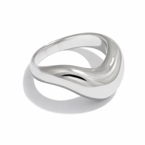 May include: A polished silver-toned ring featuring a smooth, continuous, and undulating wave-like band. The metal surface is highly reflective, creating soft highlights and shadows along the curved, organic shape of the jewellery piece.