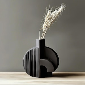 May include: A contemporary black vase with a geometric design. The vase has a half-circle with vertical lines and a curved section. It contains dried wheat stalks, creating a minimalist aesthetic. The vase is approximately 25 cm tall.
