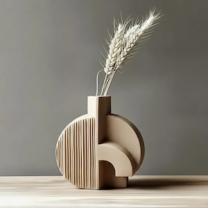 May include: A beige ceramic vase with a geometric design, featuring a half-circle with vertical lines and a curved shape. The vase holds several stalks of dried wheat. The vase is on a wooden surface against a grey background.