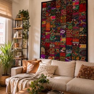 Puede incluir: Un gran tapiz rectangular que presenta un vibrante mosaico de cuadrados de tela bordados en varios colores con patrones intrincados, exhibido sobre un sofá seccional de color crema con varios cojines y una manta texturizada.