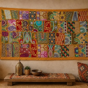 Puede incluir: Un tapiz rectangular que presenta un mosaico de paneles de tela multicolores con bordados intrincados, patrones florales, motivos de cachemira y pequeños detalles de espejos reflectantes, enmarcado por un borde de tela amarillo mostaza.