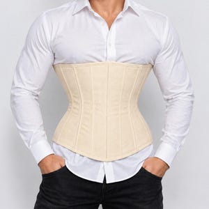 May include: A beige underbust corset featuring vertical paneling and a structured waist-cinching design, worn over a crisp white long-sleeved button-down shirt and dark trousers. The corset has a smooth finish and a curved hemline.