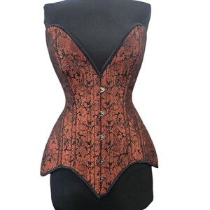 May include: A copper-colored corset with a black floral pattern. The corset has a V-neckline and is trimmed with black piping. It features a series of small buttons down the front and is displayed on a black mannequin.