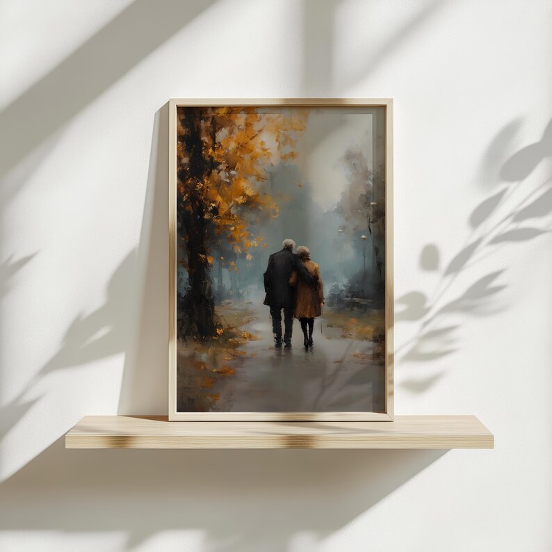 May include: A framed art print depicts an elderly couple walking on a path. The artwork features a muted color palette with shades of brown, gold, and gray. The couple is embraced, and the background shows trees with golden leaves, suggesting an autumn scene.