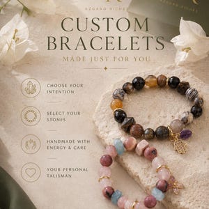 May include: Two beaded bracelets featuring natural stones in shades of brown, black, pink, and blue. One bracelet includes a gold-toned hamsa charm, while the other features a small butterfly charm. Text reads Azgard Riches Custom Bracelets.