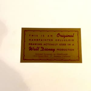 K&ouml;nnte beinhalten: Eine goldene Karte mit rotem Text, der lautet: "Dies ist eine Original-Handgemalte Celluloid-Zeichnung, die tats&auml;chlich in einer Walt Disney-Produktion verwendet wurde."
