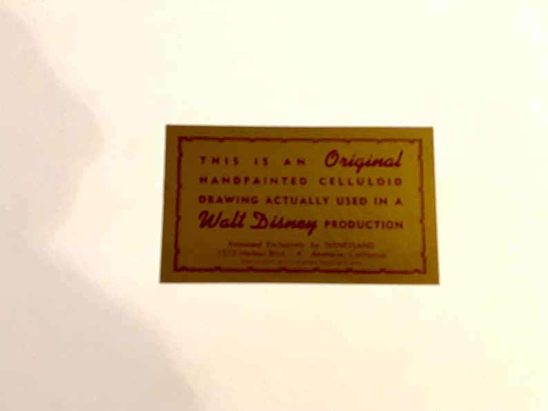 K&ouml;nnte beinhalten: Eine goldene Karte mit rotem Text, der lautet: "Dies ist eine Original-Handgemalte Celluloid-Zeichnung, die tats&auml;chlich in einer Walt Disney-Produktion verwendet wurde."