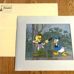 May include: A framed cartoon illustration featuring two characters. One character is a yellow bird wearing a hat and a green vest. The other character is a blue duck wearing a blue hat and a blue bow tie. The illustration is set in a forest scene with green trees and bushes. The frame is white with a light gray mat.