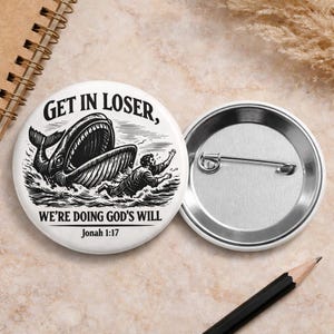 May include: White button with a black and white illustration of a whale swallowing a person. The text on the button reads "GET IN LOSER, WE'RE DOING GOD'S WILL Jonah 1:17". A silver pin back is visible.
