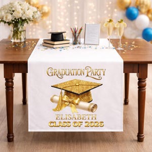 Könnte beinhalten: Weißer Tischläufer für eine Abschlussfeier mit goldenem Text und Grafiken. Der Läufer zeigt die Worte "Graduation Party", einen goldenen Glitzer-Studentenhut, ein Diplom und den Namen "Elisabeth Class of 2026".