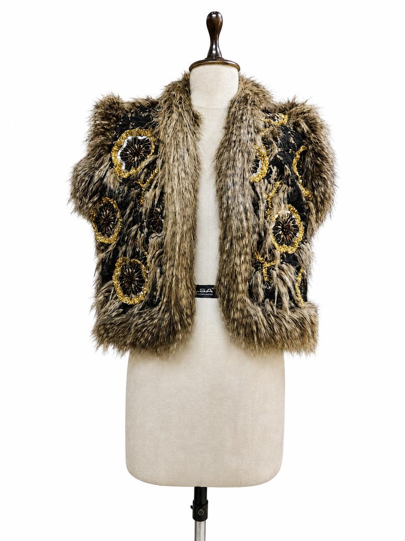 May include: A sleeveless vest featuring a black base with long, shaggy brown and tan faux fur trim along the edges. The front panels are decorated with circular floral-like patterns made of gold sequins and dark brown beads throughout the fabric.
