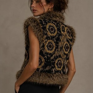 May include: A sleeveless vest featuring a black base with intricate gold circular embroidery and beadwork. The garment is trimmed with brown faux fur along the collar, armholes, and hemline, creating a textured appearance with a dark color palette.