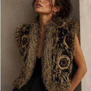 May include: A sleeveless vest featuring a black base with intricate gold sequin floral embroidery and a thick, textured brown faux fur trim along the collar, armholes, and hemline. The garment is worn over a simple black top and black trousers.