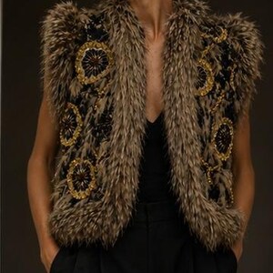 May include: A sleeveless vest featuring a black base with textured brown faux fur trim along the edges and shoulders. The garment is adorned with circular gold and black beaded floral embroidery patterns throughout the front panels.