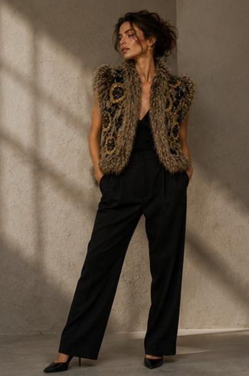 May include: A sleeveless vest featuring a textured, shaggy brown faux fur finish with dark circular embroidered patterns, worn over a black V-neck top and black wide-leg trousers, paired with black pointed-toe heels.