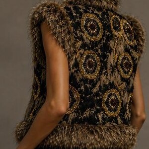 May include: A sleeveless vest featuring a black base with intricate gold and brown circular embroidery patterns. The garment is trimmed with thick, textured brown faux fur along the collar, armholes, and hemline, providing a layered appearance.
