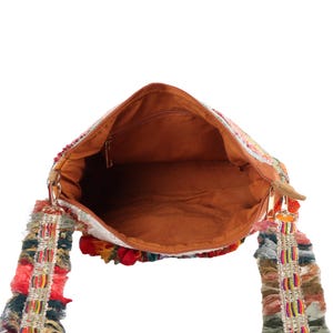 May include: Open view of a colorful shoulder bag with a brown interior. The bag features a zipper closure and decorative fringe on the straps. The exterior is adorned with a mix of vibrant colors, including red, green, and yellow.