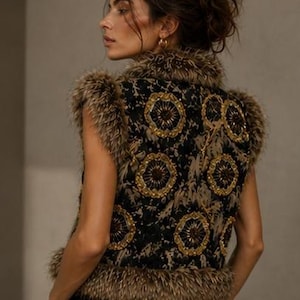 May include: A sleeveless vest featuring a black base with a tan abstract pattern and circular gold beaded embellishments. The garment is trimmed with brown faux fur along the collar, armholes, and hemline, creating a textured appearance.