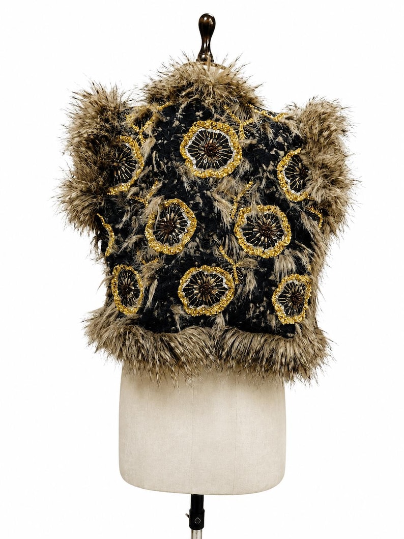 May include: A sleeveless vest featuring a black base with a textured, shaggy brown and tan faux fur trim along the edges and collar. The garment is decorated with multiple circular floral motifs embroidered with gold and dark brown beads.