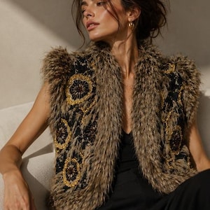 May include: A sleeveless vest featuring a black lace base with intricate gold and dark brown circular embroidery. The garment is trimmed with long, textured brown faux fur along the collar, armholes, and front edges, creating a layered appearance.