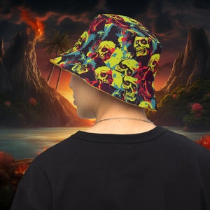 May include: A black bucket hat with a colorful pattern of skulls and abstract shapes. The hat is worn by a person standing in front of a sunset scene with a volcano in the background.