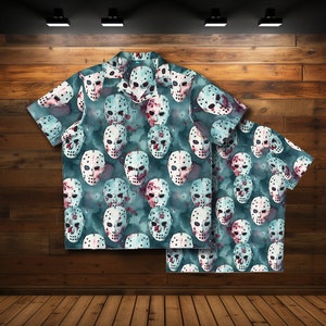 Puede incluir: Una camisa de manga corta con botones de color azul verdoso con un patrón repetido de máscaras de hockey blancas con salpicaduras de pintura roja.