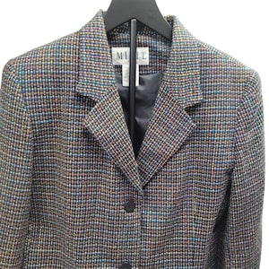 Könnte beinhalten: Ein mehrfarbiger Tweed-Blazer mit Reverskragen und drei dunklen Knöpfen. Der Blazer hat ein klassisches Design und hängt an einem schwarzen Kleiderbügel. Das Etikett im Blazer lautet "MI IT".